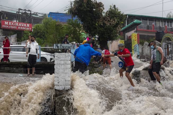 People help each other cross a street amid sudden gush of water during flash floods after heavy monsoon rains in Bhagsunag, a popular tourist town in Himachal Pradesh, India, Monday, July 12, 2021. (AP Photo/Ashwini Bhatia)