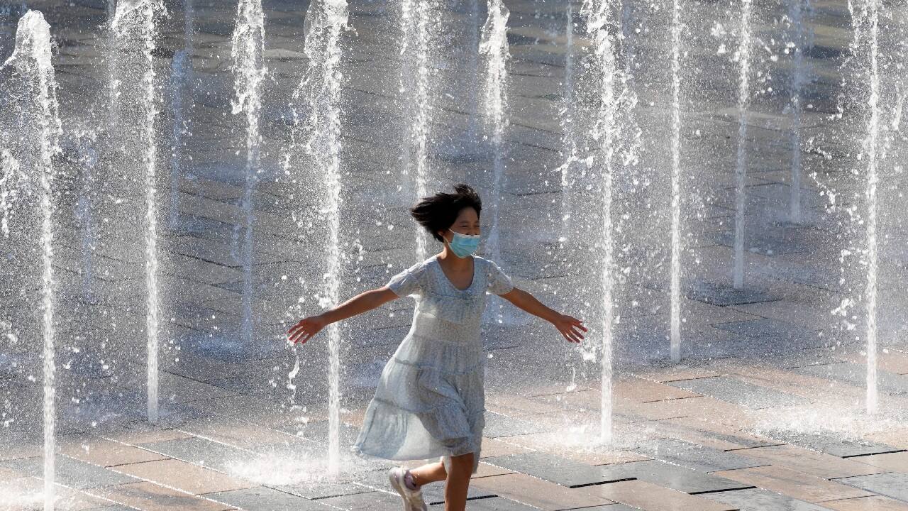 A girl wearing a mask to help curb the spread of the corona virus runs through a fountain in Beijing, China, August 26. (Image: AP)