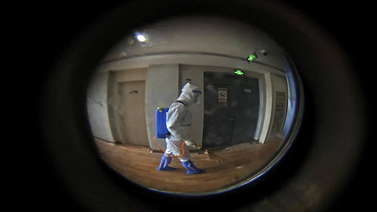 Seen through a door peephole, a medical worker wearing a protective clothing disinfects the corridor of a hotel used for foreigners to stay during a period of health quarantine in Shanghai, China, Thursday, Aug. 12, 2021. More than 30 Chinese officials have been fired or received other punishments over accusations they failed to respond properly to the latest surge of the coronavirus in the country. (AP Photo/Andy Wong)