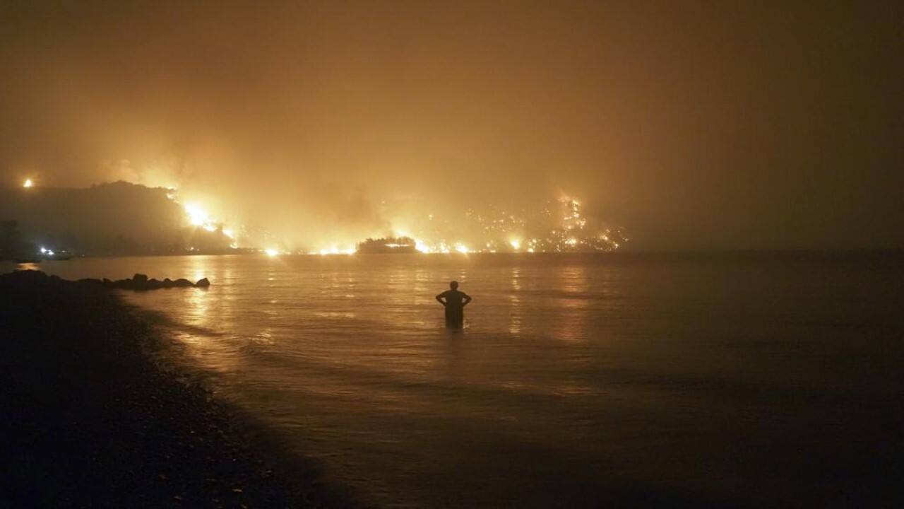 A man watches the flames as wildfire approaches Kochyli beach near the village of Limni, Greece, on the island of Evia, about 160 kilometers (100 miles) north of Athens, late Friday, Aug. 6, 2021, as wildfires raged uncontrolled through Greece and Turkey. (Image: AP)