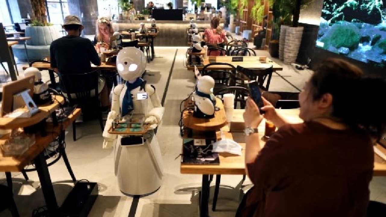 At a Tokyo cafe, Michio Imai greets a customer, but not in person. He's hundreds of kilometres away, operating a robot waiter as part of an experiment in inclusive employment. (Image: AFP)
