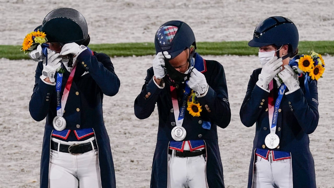 A last-minute rule change allowed athletes to remove their masks for a podium photo-op with their medals, but the face coverings had to be quickly restored. Thus the awkwardness as American dressage riders Adrienne Lyle, Steffen Peters and Sabine Schut-Kery fiddled to get their masks back in place. (Image: AP)