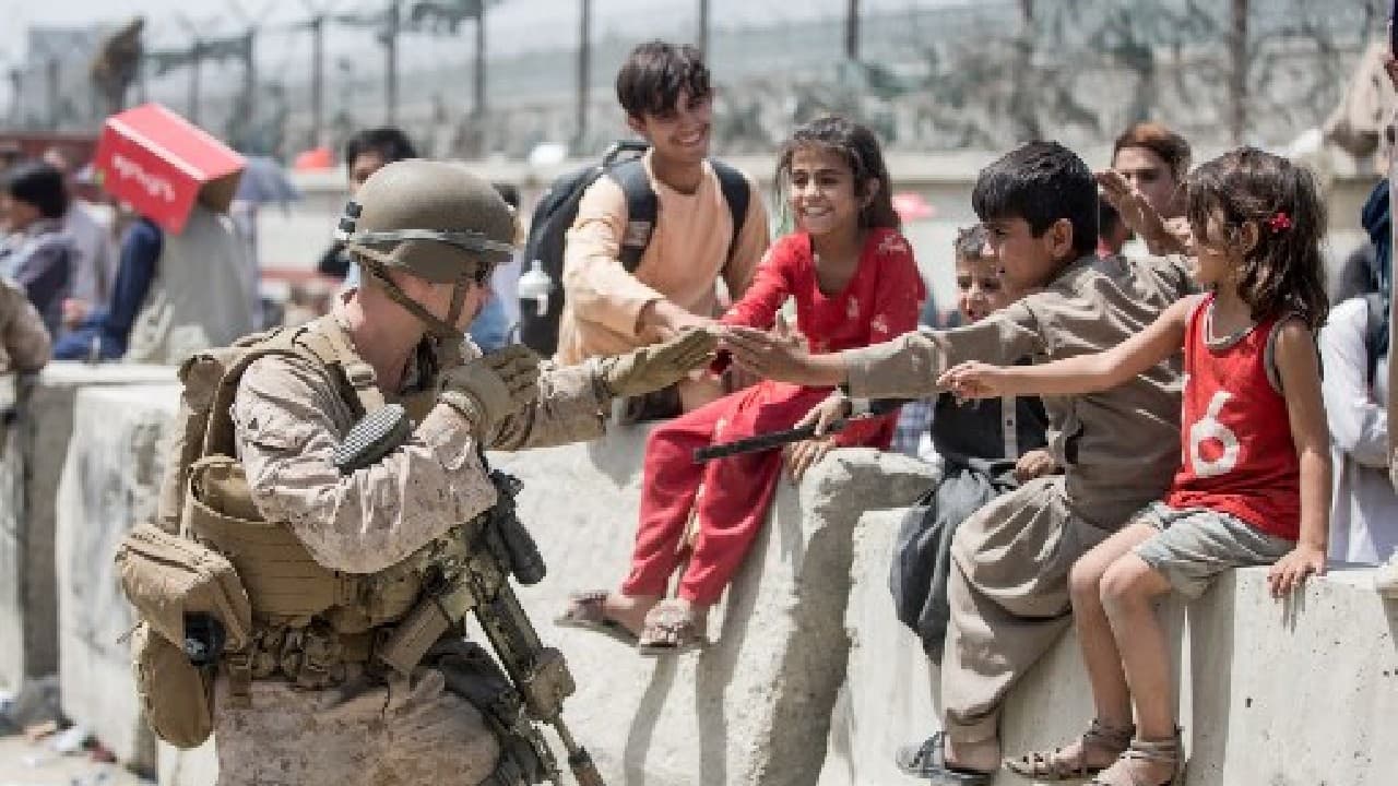 A US Marine plays with children waiting to be processed during an evacuation at Hamid Karzai International Airport in Kabul on August 20. (Image: US Central Command Public Affairs / AFP)