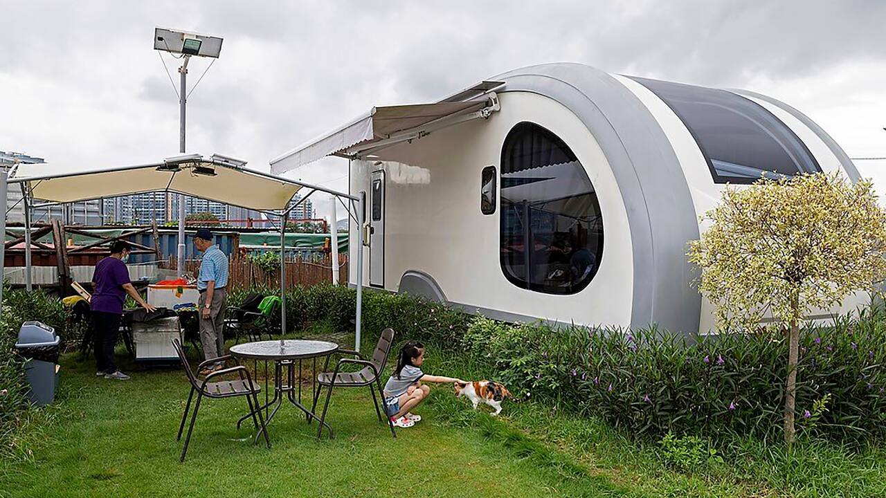 A couple cleans up the table outside the signature stargazing caravan of Park Nature, a glamping site that offers luxury caravans packages in Hong Kong on August 14, 2021, while their granddaughter plays with a cat in Hong Kong. (AP Photo/Matthew Cheng)