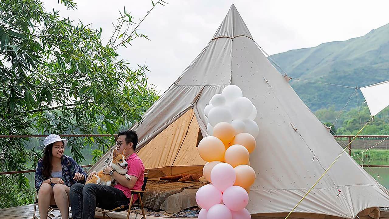 A young couple with their dog spend their time outside an Indiana-style tent at We Camp, a glamping site located in Yuen Long, Hong Kong on August 19, 2021. (AP Photo/Matthew Cheng)