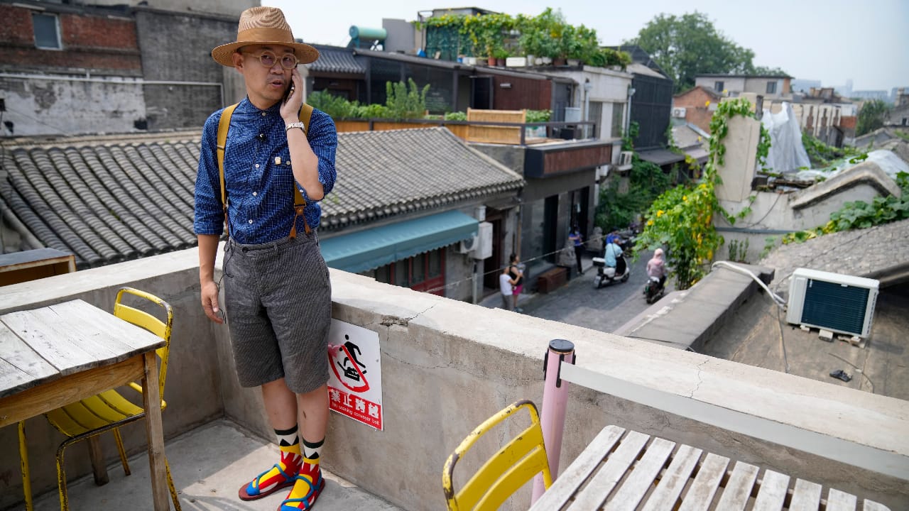Cafe owner Phil Ma talks on his phone as he stands on the roof of his shop in a neighborhood popular with tourists in central Beijing. (AP Photo/Mark Schiefelbein)