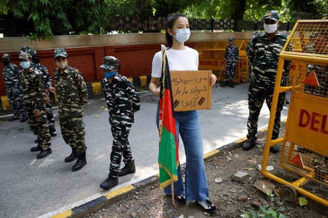 An Afghan woman holds a placard as she stands next to Indian security forces during a protest demanding international community to help Afghan refugees, in New Delhi, India, August 23, 2021. REUTERS/Adnan Abidi - RC2XAP9QS1ON