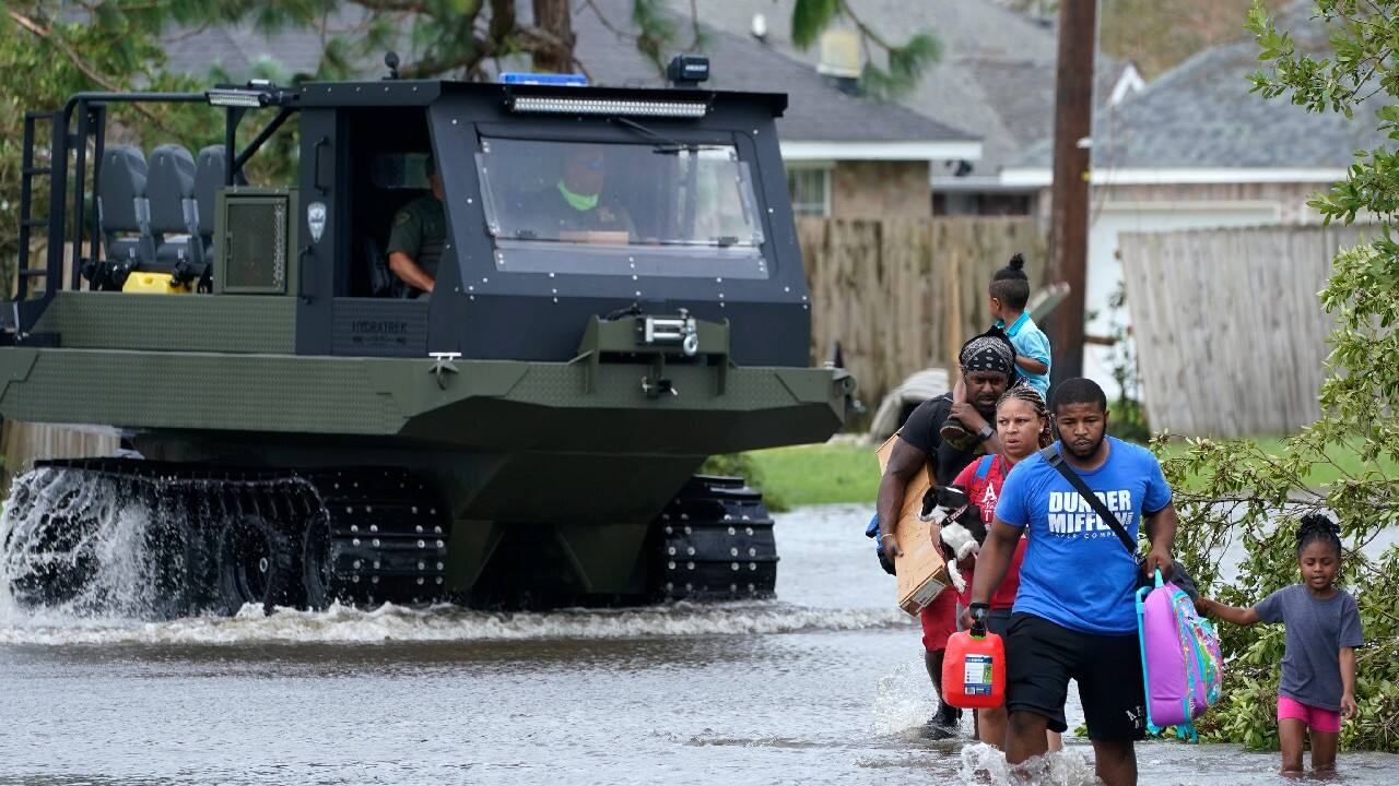 Michael Thomas, back, carries his daughter Mikala, out of his flooded neighborhood while a high water rescue vehicle moves past after Hurricane Ida moved through, August 30, in LaPlace, La. (Image: AP)