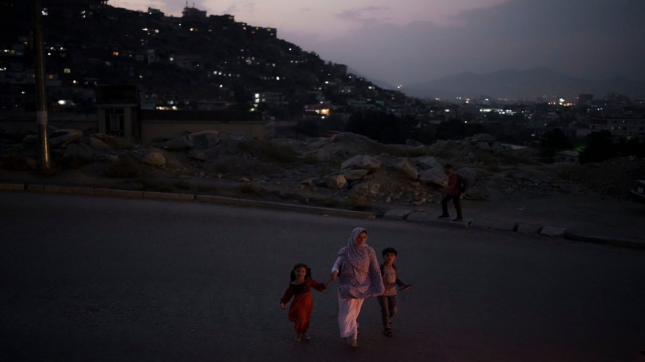 As night fell, a woman crossed the street holding the hands of a little girl and boy, the lights of Kabul dotting across the hills behind them. (AP Photo/Felipe Dana)