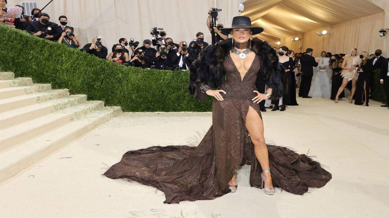 Superstar Jennifer Lopez chose to sizzle in a custom Ralph Lauren high-leg slit, accessorized with faux fur, and a cowgirl hat as her dress to the Met Gala 2021. 