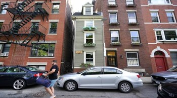 FILE— In this Aug. 13, 2021 file photograph, a man walks by Boston's famous Skinny House, at center, after it was listed for sale for $1.2 million. The sale of the home was closed Thursday Sept. 16, 2021 for $1.25 million, according to Zillow. The home "received multiple offers and went under agreement for over list price in less than one week," real estate agency CL Properties posted on Facebook. (AP Photo/Elise Amendola, File)
