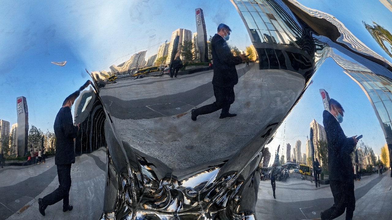 A man wearing a face mask to help curb the spread of the coronavirus is reflected on an art installation on display outside a shopping mall in Beijing, October 17. (Image: AP)