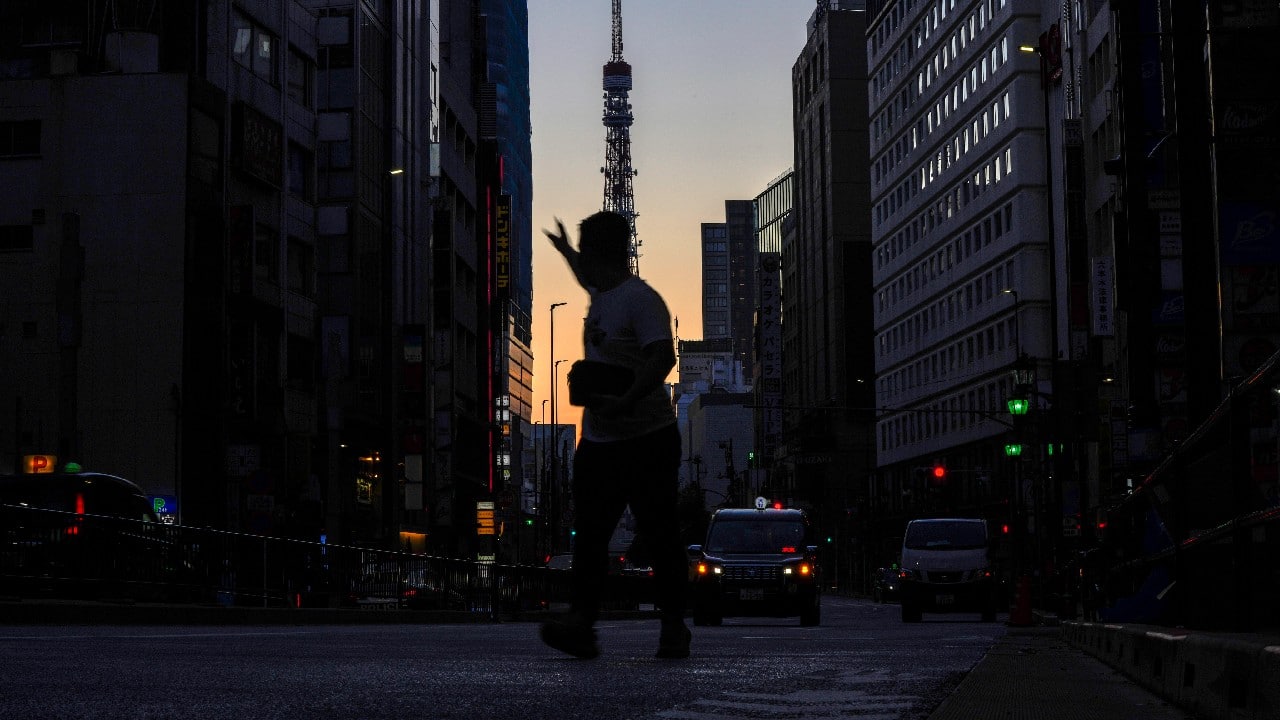 A man hails a taxi in Roppingi neighborhood, an entertainment district, in Tokyo, October 20, as Tokyo Tower is silhouetted against the sunrise colored sky in the background. Daily new COVID-19 cases have plummeted from a mid-August peak of nearly 6,000 in Tokyo, with caseloads in the densely populated capital now routinely below 100, an 11-month low. (Image: AP)