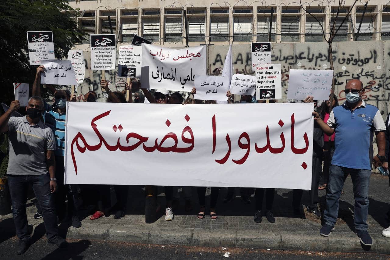 Customers hold a banner with Arabic that reads: "Pandora (Papers) exposed you," during a protest in front of the Central Bank in Beirut, Lebanon, Wednesday, Oct. 6, 2021. Dozens of Lebanese gathered outside a bank in Beirut's downtown demanding that they be allowed to withdraw their deposits that have been blocked amid Lebanon's severe financial and economic crisis. (AP Photo/Bilal Hussein)