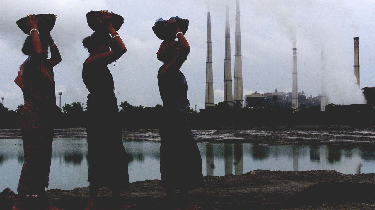 Female labourers carry small pieces of coal deposit from liquid ash generated from a thermal power plant (background) in Kolaghat in West Bengal. (PC-Reuters)