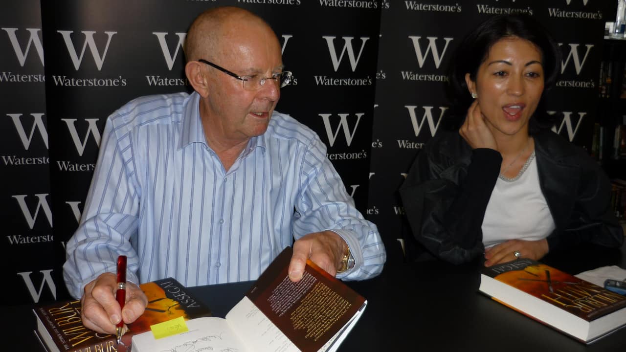 South African author Wilbur Smith signing copies of 'Assegai' in London in April 2009. Smith passed away on November 13, 2021. (Image by Vesi Libra via Wikimedia Commons 3.0)