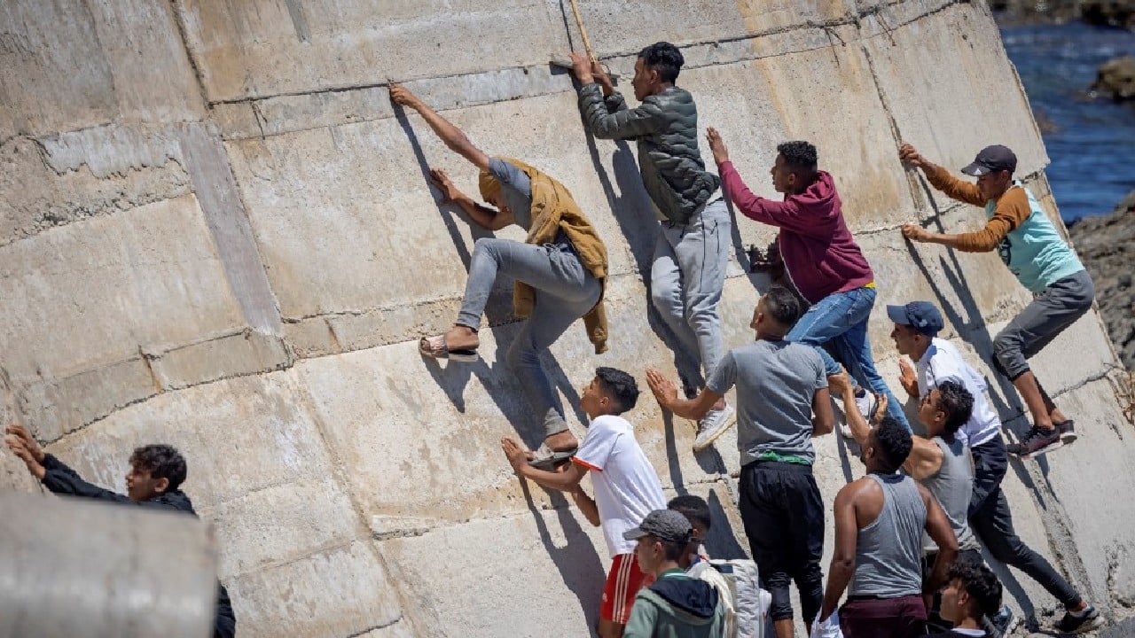 Migants climb a sea wall in the northern town of Fnideq after attempting to cross the border from Morocco to Spain's North African enclave of Ceuta on May 19. Spain stepped up diplomatic pressure on Rabat as its prime minister flew into Ceuta, vowing to &quot;restore order&quot; in the North African enclave after a record 8,000 migrants reached its beaches from Morocco. (Image: AFP)