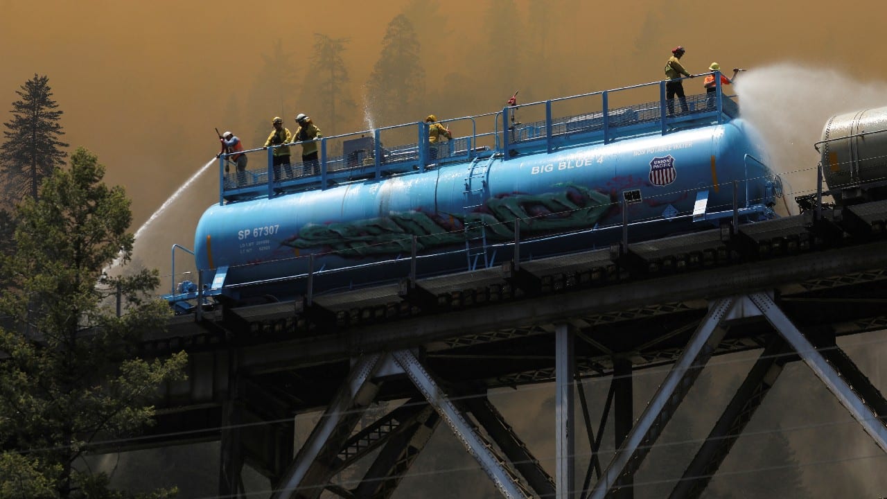 Firefighters spray water from a fire train to hot spots along the tracks over Rock Creek Bridge as the Dixie Fire grows in Plumas National Forest, California, U.S., July 15. (Image: Reuters)