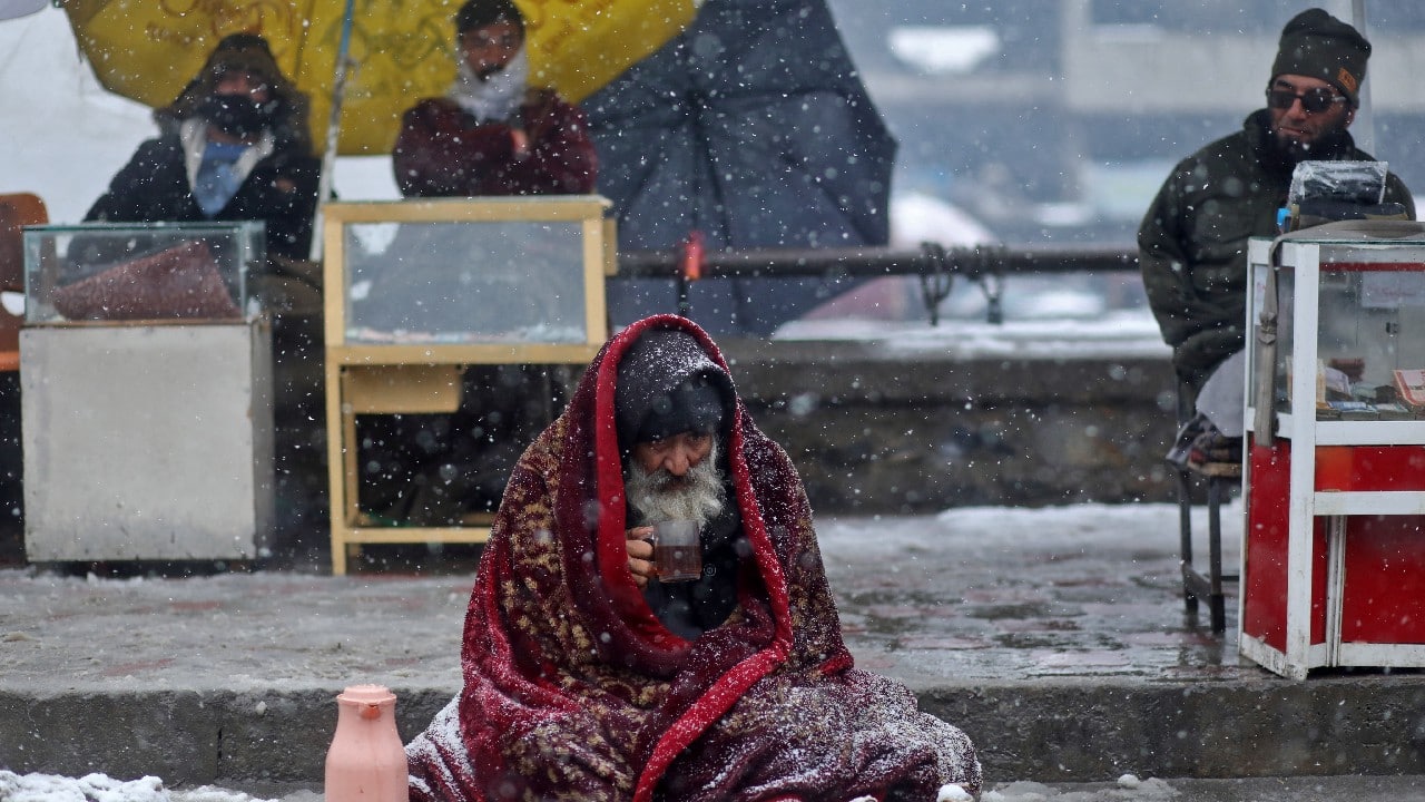 An elderly man drinks tea as he sits alongside a road during a snowfall in Kabul, Afghanistan, January 3. (Image: Reuters)