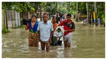 People wade through flood waters in Solmara of Nalbari district, in India's Assam state on June 19, 2022.
