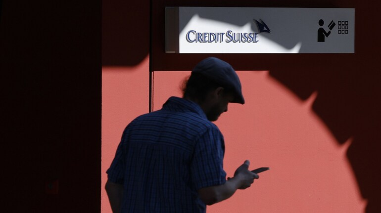 A pedestrian browses a smartphone by a Credit Suisse Group AG bank branch in Zurich, Switzerland, on Thursday, March 24, 2022. Credit Suisse warned it may need to set aside more funds for legal costs as a result of an expected Bermuda court ruling finding it liable for potentially more than $500 million in a case involving a local insurance unit.