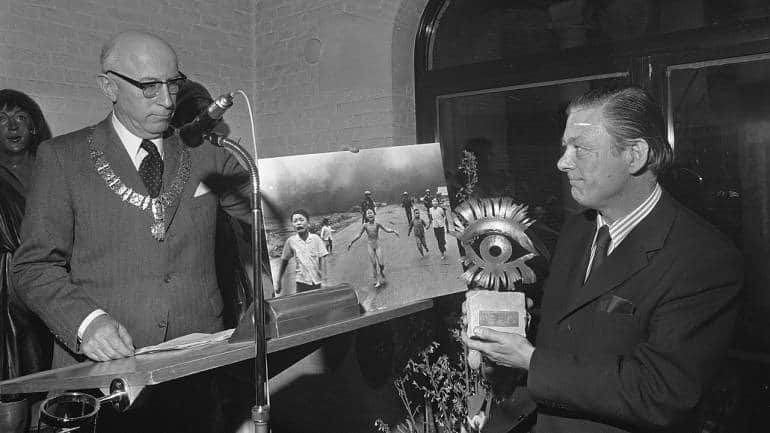 Peter Gail, AP representative, receives the Golden Eye Award on behalf of Nick Ut from Ivo Samkalden, Mayor of Amsterdam, at Amsterdams Historisch Museum on 4 April 1973. 'Accidental Napalm' can be seen to the right of the podium. (Photo by Rob Mieremet / Anefo via Wikimedia Commons)
