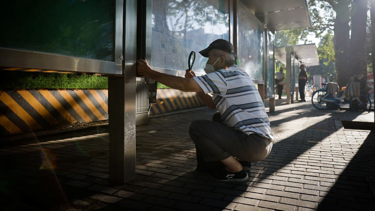 A man uses a magnifying glass to read a newspaper at a public display wall in Beijing, China, July 28. (Image: Reuters)