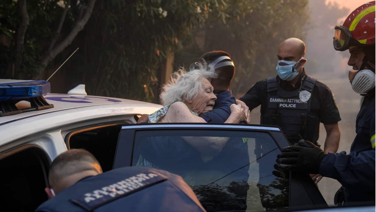 Firefighters and policemen evacuate a woman from her home in Penteli, Greece, Tuesday, July 19, as a wildfire threatened mountainside suburbs northeast of Athens. 