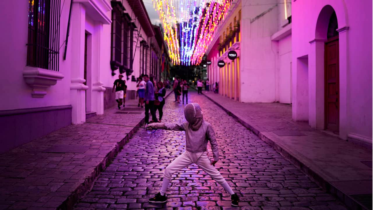 A young fencer strikes a pose for her parents as they take photos of her in downtown Caracas, Venezuela, Sunday, July 24.
