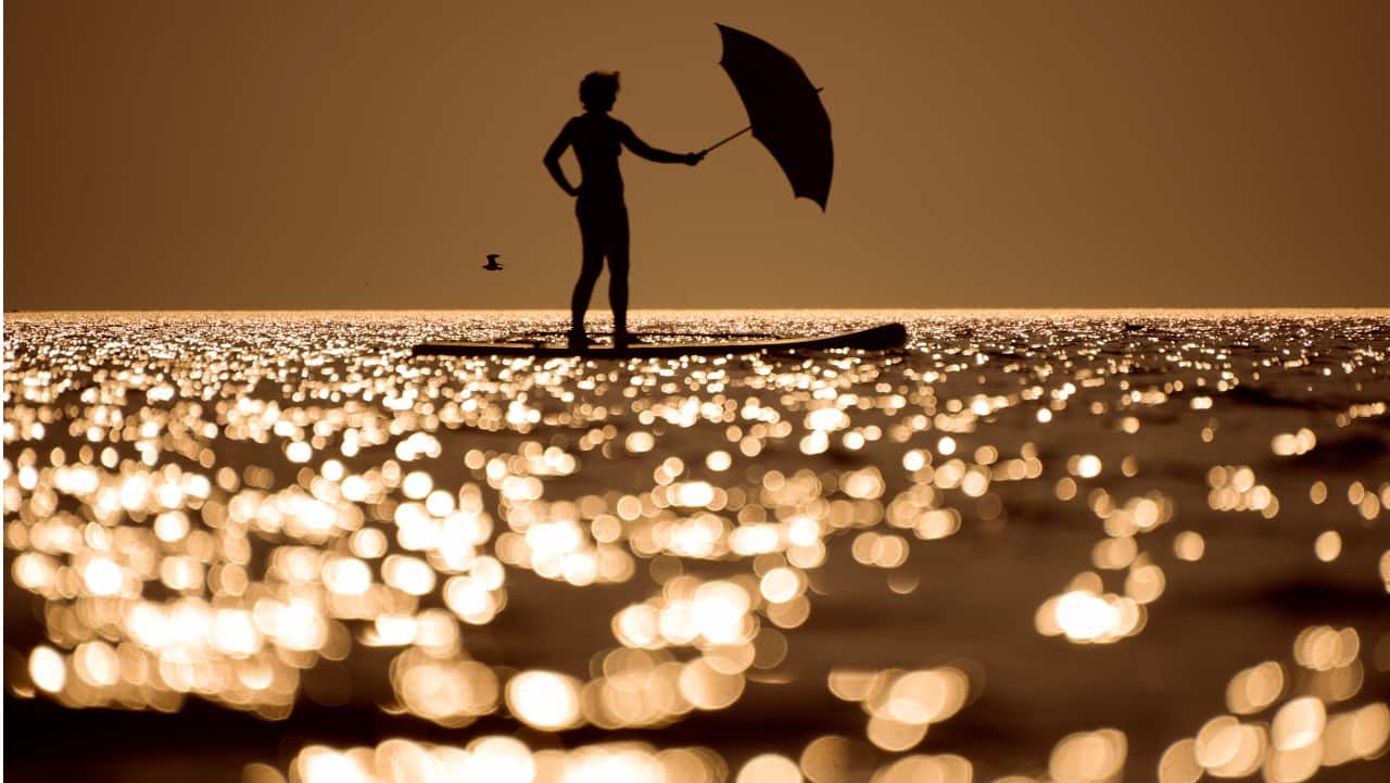 A woman steers her stand-up paddle board using an umbrella as a sail at Ladoga lake near the city of Olonets, 300 kilometers (186 miles) north-east of St. Petersburg, Russia.