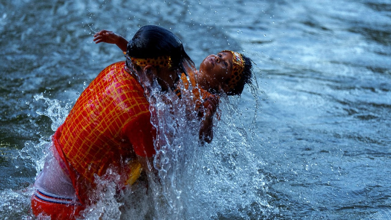 A Hindu devotee takes a holy dip with his child before collecting water from the Bagmati River during the Bol Bom pilgrimage at Sudarijaal, on the outskirts of Kathmandu, Nepal, August 8. During this pilgrimage, devotees collect water from the Bagmati River and walk miles barefooted before offering the same at the Pashupatinath Shiva temple in Kathmandu. (Image: AP)