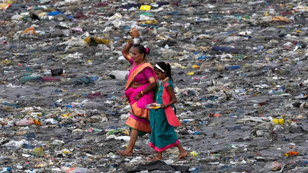 Members of the fishing community make their way through plastic waste on the beach to offer coconut to the sea on the occasion of Narli Pournima, or coconut festival in Mumbai, India, August 11. (Image: AP)
