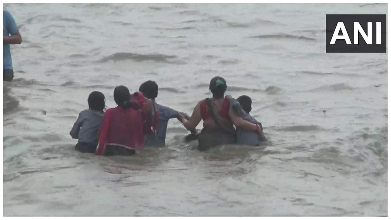 Several people are seen making their way through waist-deep water. (Image: @ANI/Twitter)