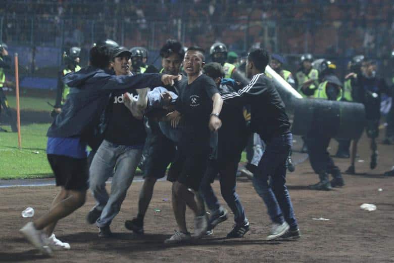 Indonesia stampede: Supporters evacuate a man hit by tear gas fired by police during a riot after a soccer match between at Kanjuruhan Stadium, Malang, East Java province, Indonesia, October 2. The stampede was among the world's worst sporting disasters, as hundreds of soccer fans tried to flee a stadium riot leaving at least 131 people dead. (Image: Antara Foto/Ari Bowo Sucipto)