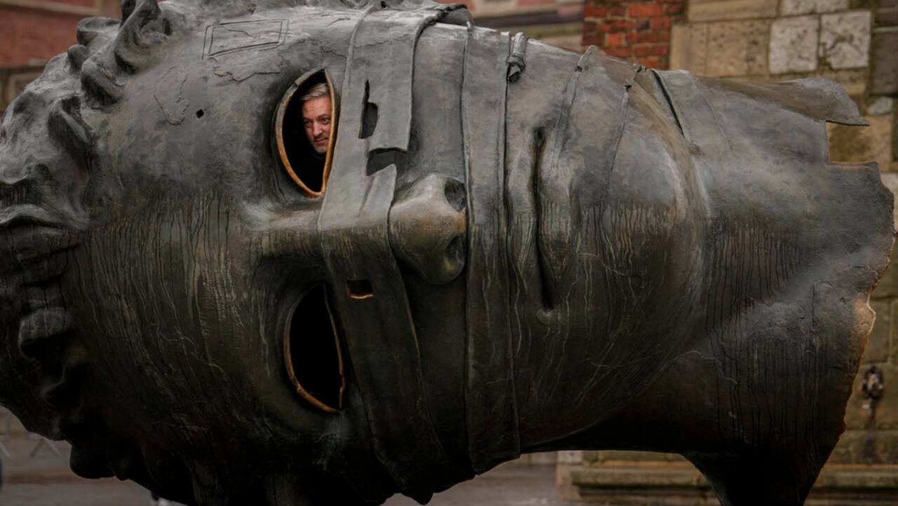 A man peers from a depiction of Eros, the Greek god of love, by Polish sculptor Igor Mitoraj downtown Krakow, Poland, Thursday, Nov. 10, 2022. Eros Bound, an artwork said to symbolize the decay of civilizations is placed in the 13th century main square of the old city area of Krakow. 