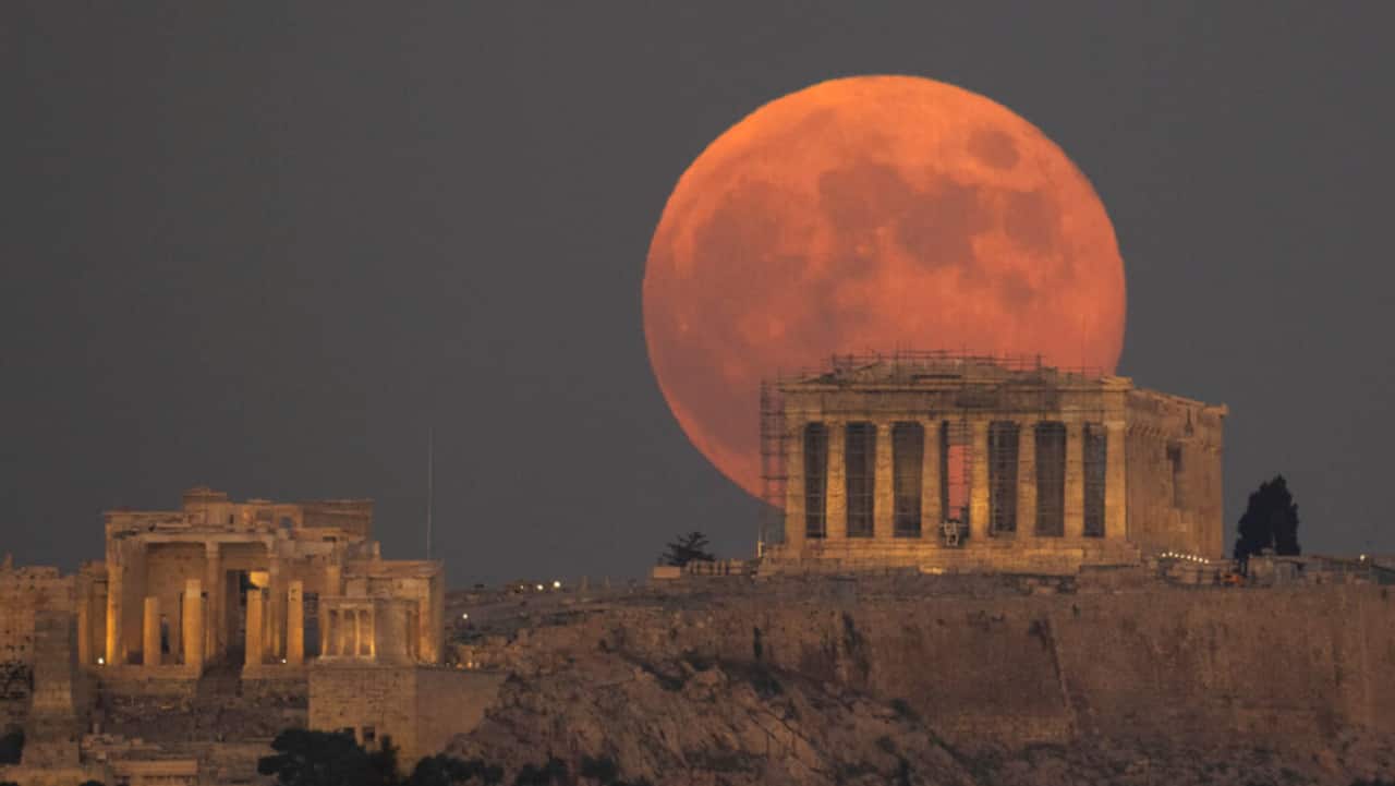 The full moon rises behind the Acropolis hill and the ancient Parthenon Temple, in Athens, Greece.