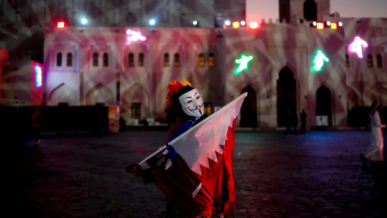 A woman with a mask holds a flag from Qatar at Katara Cultural Village in Doha, Qatar. (Image: AP)