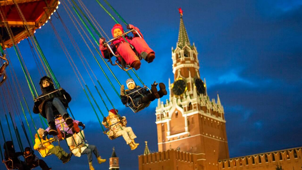 Children and their parents ride a carousel at a Christmas Market set up in Red Square decorated for the New Year and Christmas festivities with the Spasskaya Tower in the background, in Moscow, Russia.