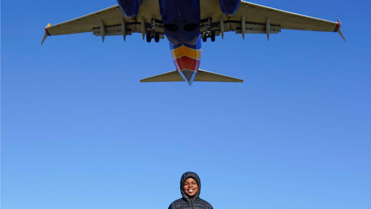 Orin Okubadejo, 12, of Maryland, poses for a photo for his family as a Southwest Airlines plane flies low over Gravelly Point on approach to Ronald Reagan Washington National Airport in Arlington, Va.