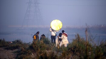 A bride and groom pose for a pre wedding photoshoot with a light man holding reflector at Yamuna Ghat, kashmiri Gate in Delhi.  Photographer: Pradeep Gaur/SOPA Images/LightRocket/Getty Images