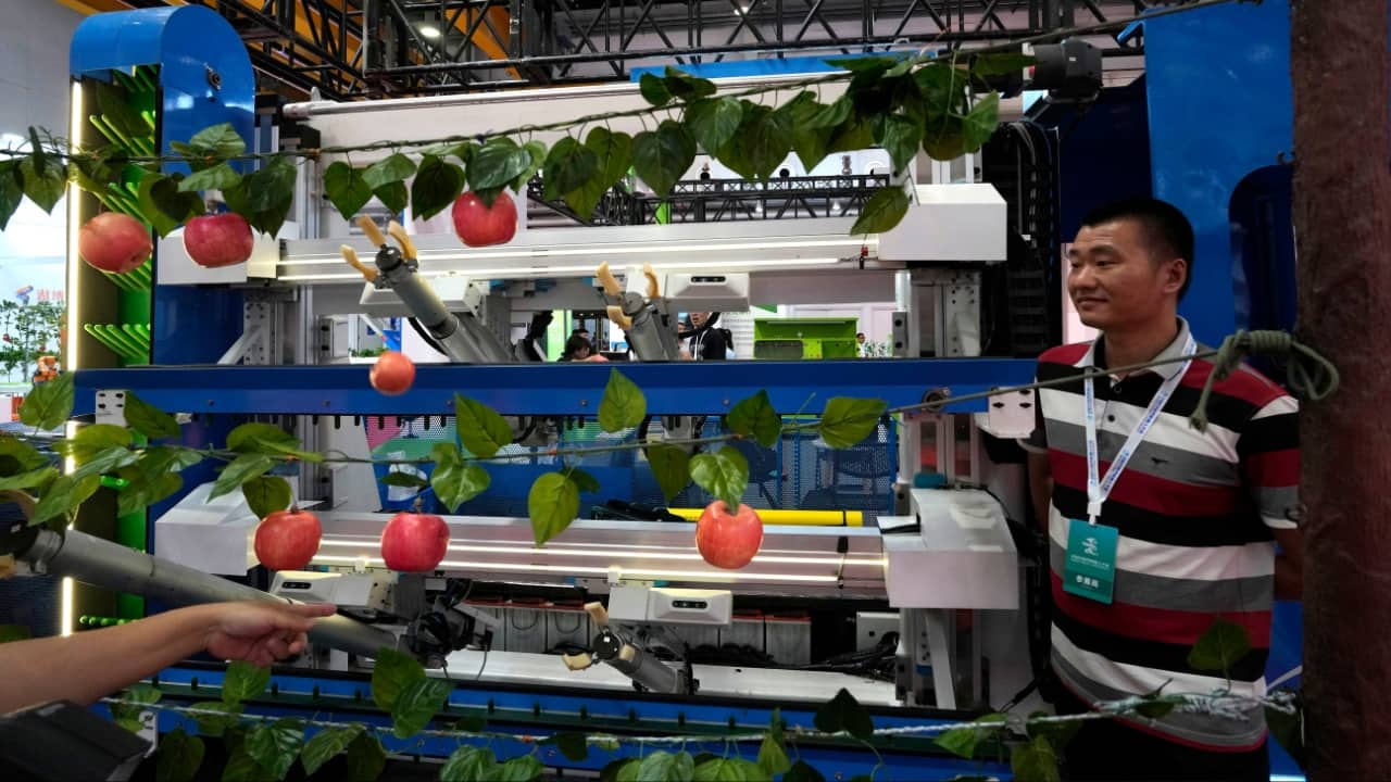 A worker stands next to apples harvesting robot displayed at the annual World Robot Conference held at the Beijing Etrong International Exhibition and Convention Center, August 16. (Image: AP)