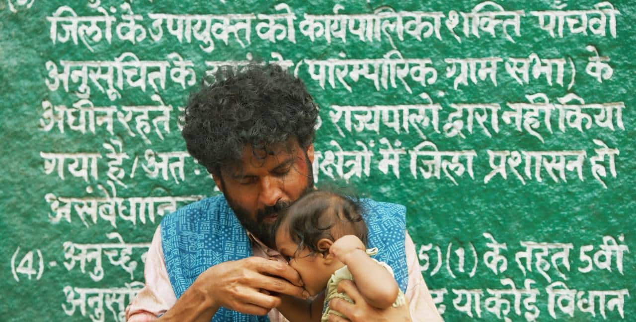 Bala while on the run, feeds Joram in front of a stony fixture with the Constitution writ large over it.
