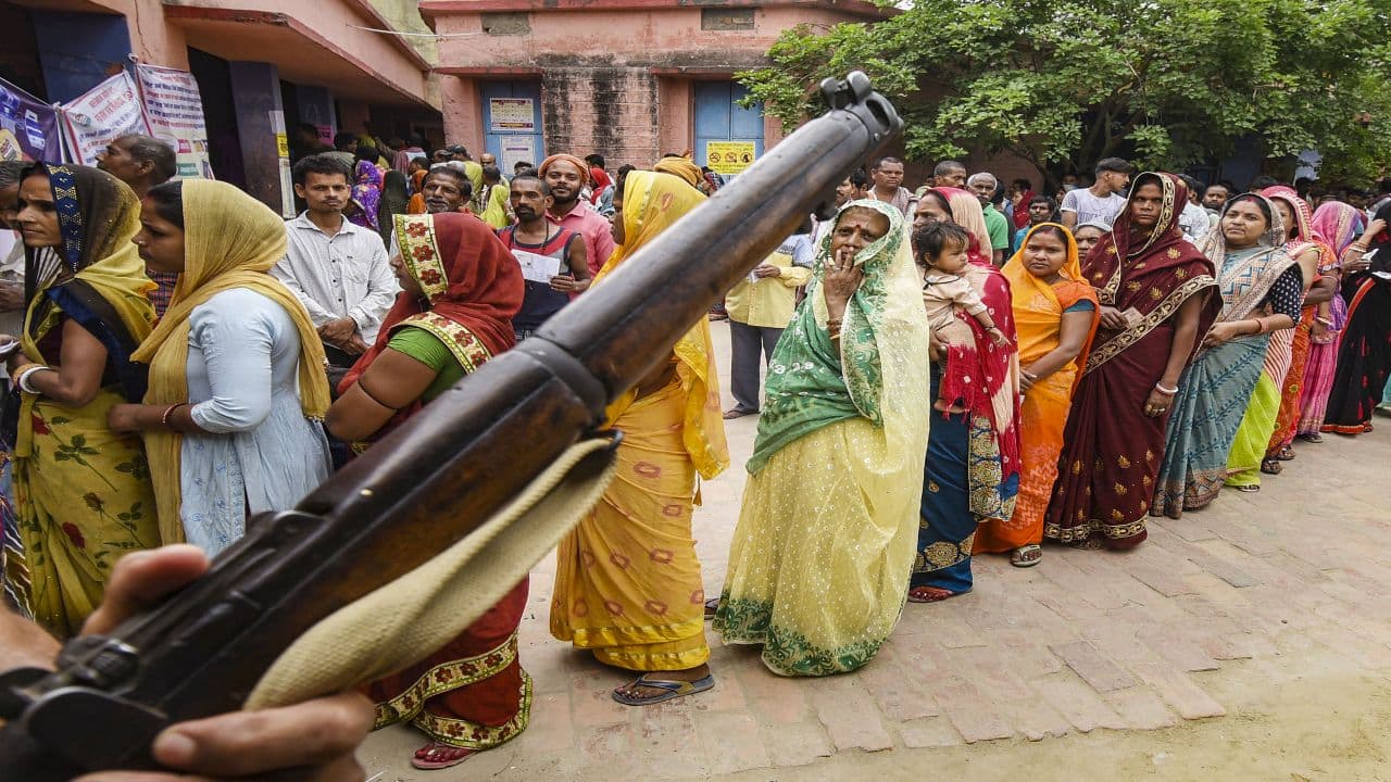 Khagaria: A security personnel stands guard as voters wait in a queue at a polling station to cast their votes during the third phase of Lok Sabha polls, in Khagaria, Tuesday, May 7, 2024. (PTI Photo) (PTI05_07_2024_000077B) *** Local Caption ***