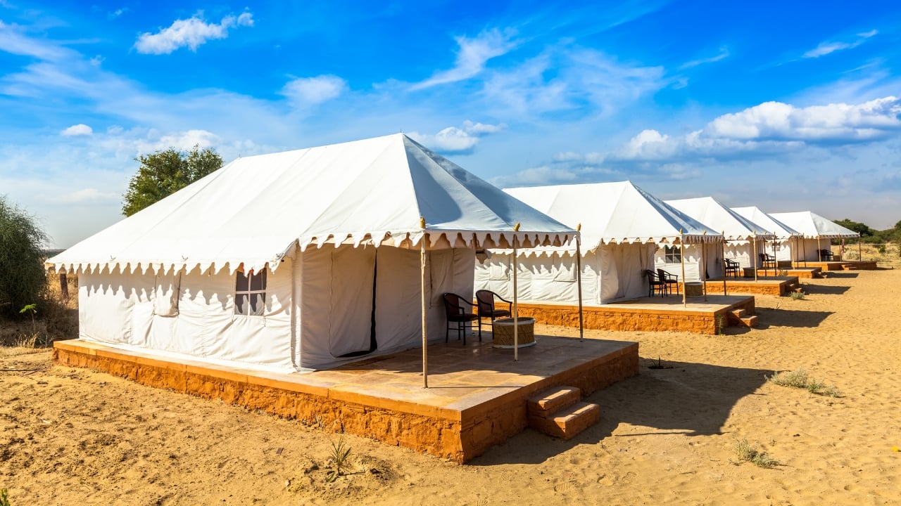 3. Jaisalmer, Rajasthan: Desert Camping Under the Stars Jaisalmer, with its expansive Thar Desert, offers a unique camping experience amidst the golden sand dunes. Settle into luxury desert camps, ride camels across the sands, and feast on traditional Rajasthani meals. As the day ends, enjoy cultural performances with Rajasthani folk music and dance, before falling asleep beneath the vast, star-filled sky. It's an adventure that brings desert magic to life. (Image: Canva)