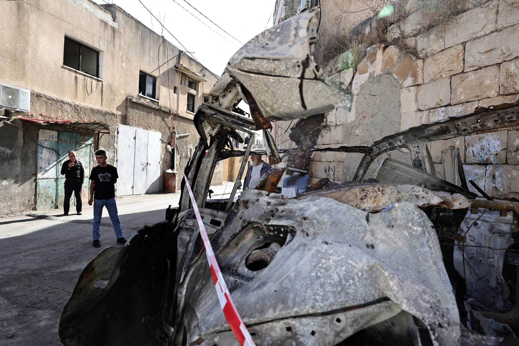 Men walk past a destroyed car in which Palestinian Shadi Zakarneh, identified by Israeli authorities as "responsible for directing and carrying out attacks in the northern West Bank area", was killed as the car was targeted during a military raid the previous day in Qabatiyah south of Jenin, on September 20, 2024. - Qabatiyah is located in the north of the West Bank, where the military has been carrying out large-scale raids since late August that the Palestinian health ministry says have left dozens dead. The military said in a statement on September 20 that four militants were killed "in an exchange of fire" in Qabatiyah, while three others were killed in an air strike on a vehicle there. (Photo by Zain JAAFAR / AFP)