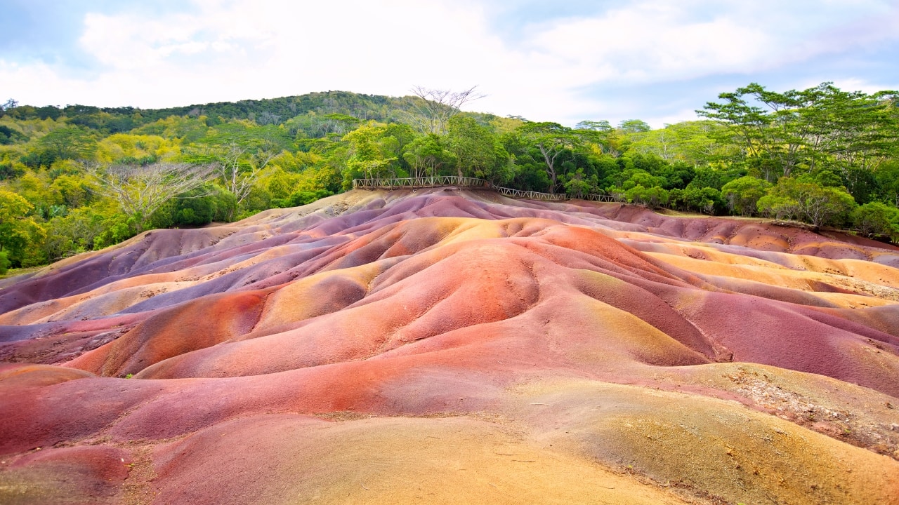 3. Explore the Seven Colored Earths in Chamarel Discover the colorful wonders of Chamarel’s Seven Colored Earths, a natural phenomenon where sand dunes in a variety of vibrant hues create a stunning landscape. It’s a must-see for nature lovers seeking a unique honeymoon experience. (Image: Canva)