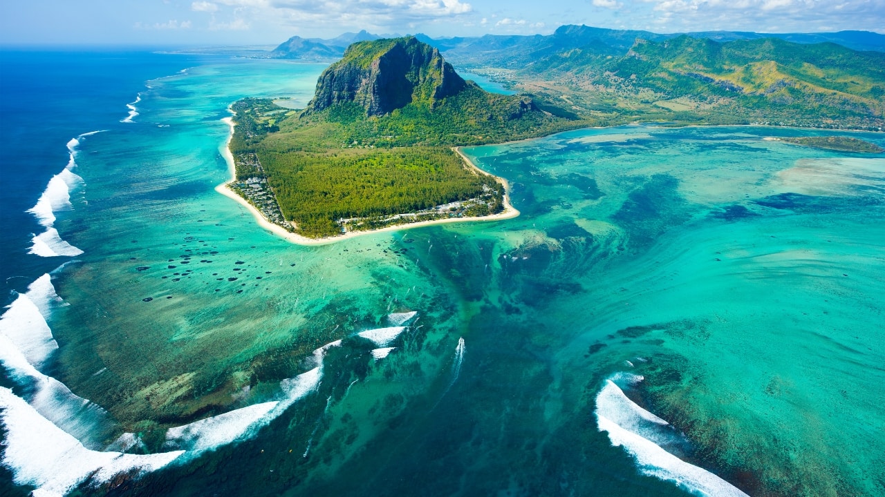 1. The &quot;Underwater Waterfall&quot; – Mauritius Imagine standing on the edge of the ocean and watching a massive waterfall plummet into the depths below. Except—it’s not a waterfall at all. This mesmerizing illusion off the coast of Mauritius is caused by sand and silt being pushed off the edge of the Mascarene Plateau by ocean currents. When viewed from above, it looks like the sea is folding in on itself, creating a breathtaking visual trick. (Image: Canva)