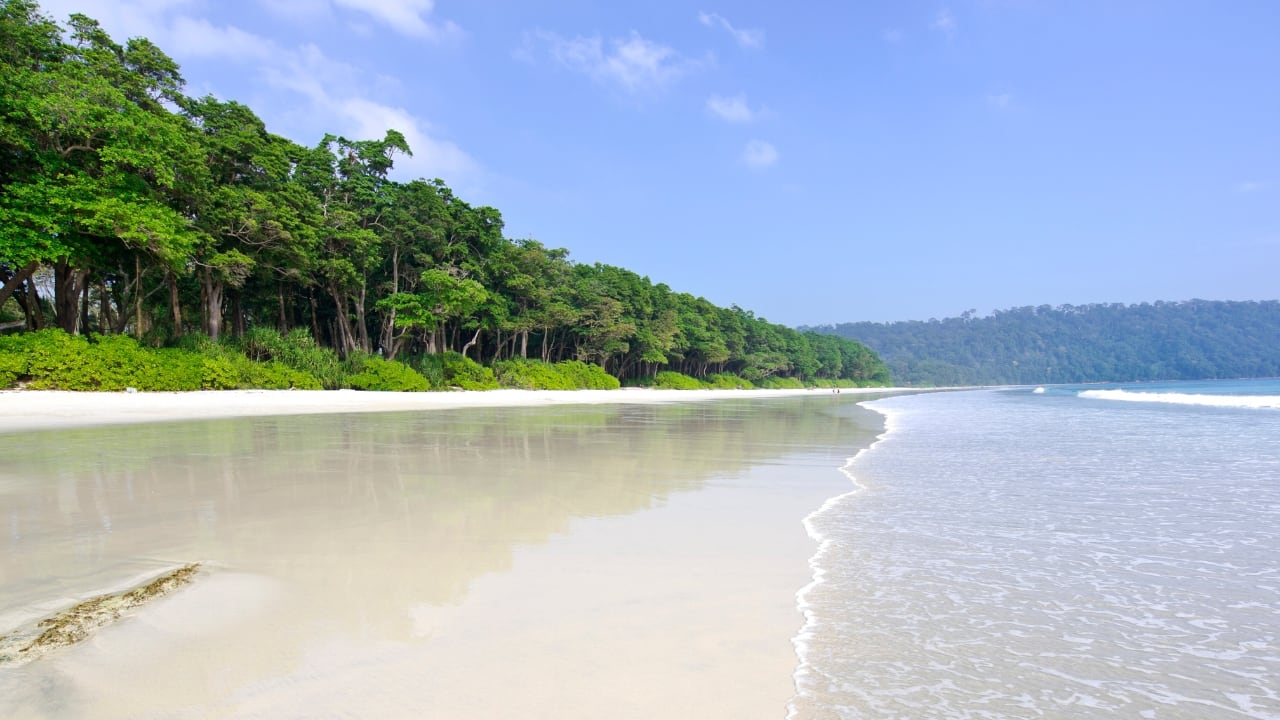 1. Radhanagar Beach – Havelock Island, Andaman &amp; Nicobar The sand is pale and soft as sifted flour; the sea, a calm expanse of azure that gathers dusk in delicate shades. Radhanagar doesn’t shout for attention. It simply waits—stoic, unspoiled, unforgettable. (Image: Canva)