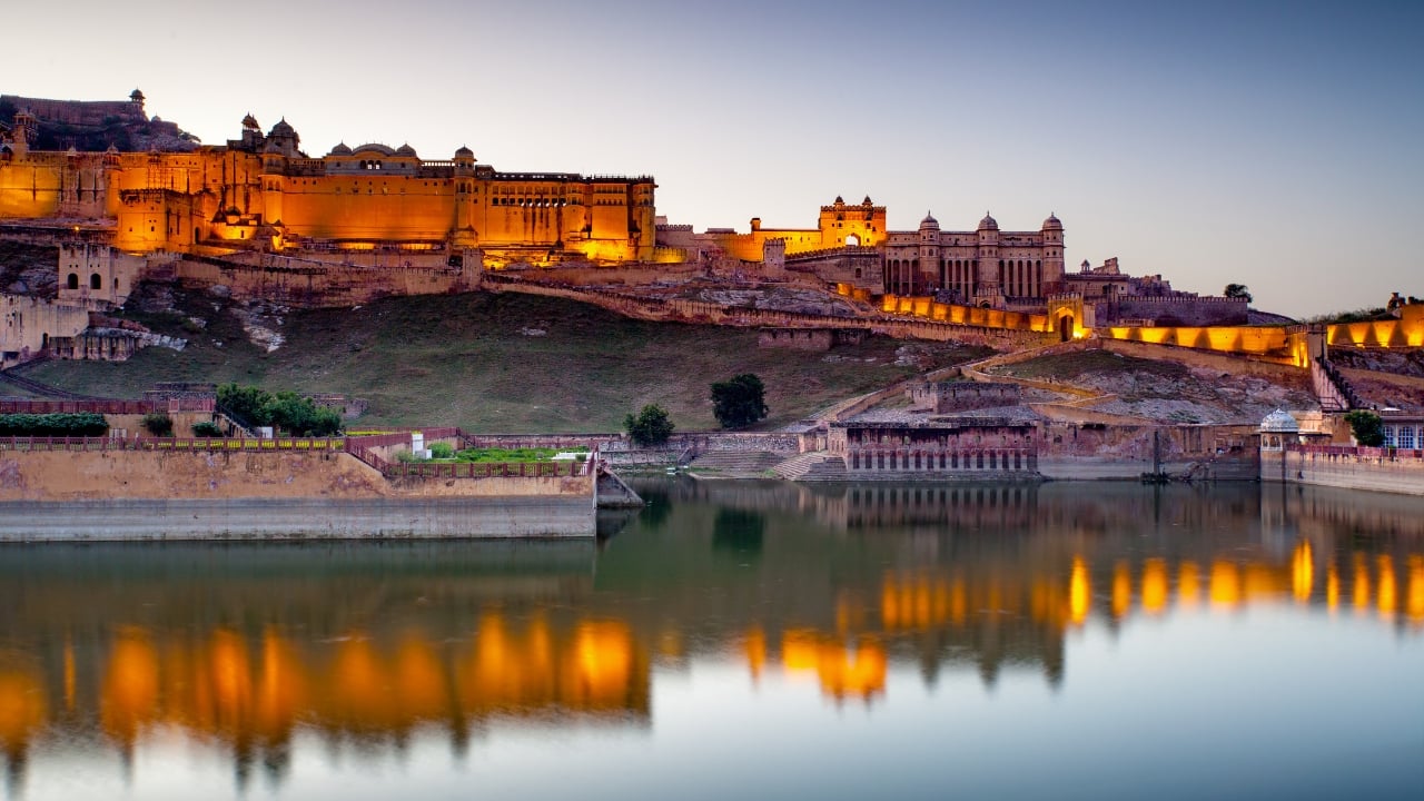 5. Amber Fort – Jaipur, Rajasthan Amber Fort wears moonlight well. The pale stone walls, once battered by the desert sun, soften and gleam in the evening hours. Reflections flicker across the Maota Lake, and the fort's silhouette sharpens into sculpture. On certain nights, cultural performances unfold in the open courtyards—part palace, part stage. (Image: Canva)