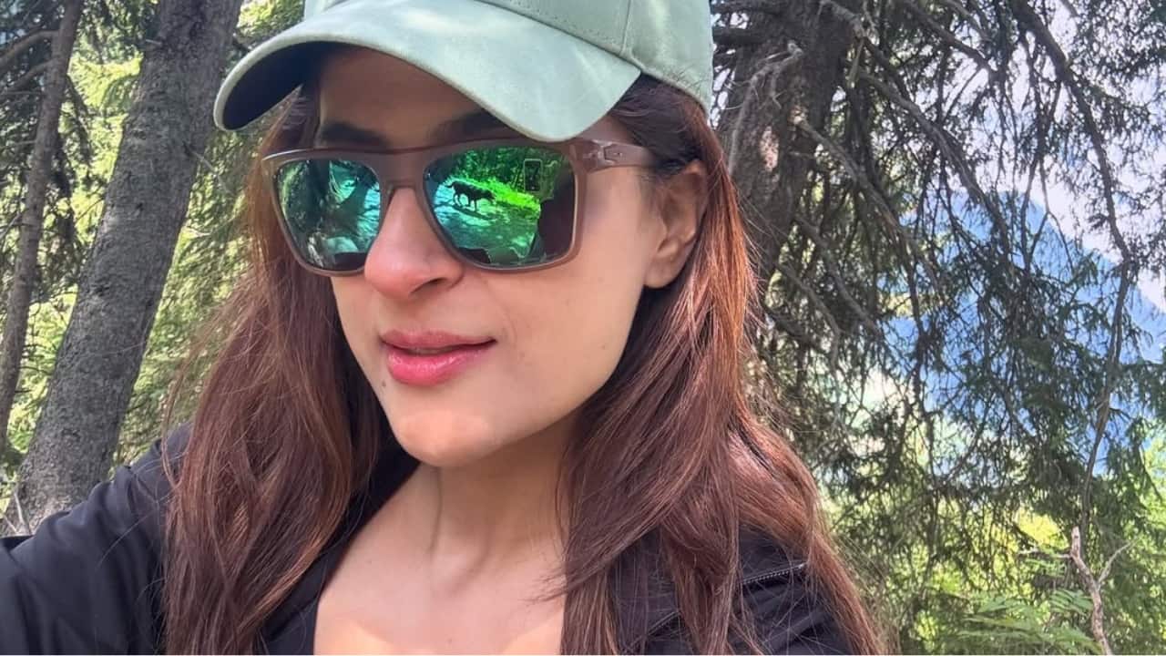 Forest pause Tahira sits calmly under the shade of tall trees, taking a quiet moment to rest. With her cap and shades on, she looks completely at ease.